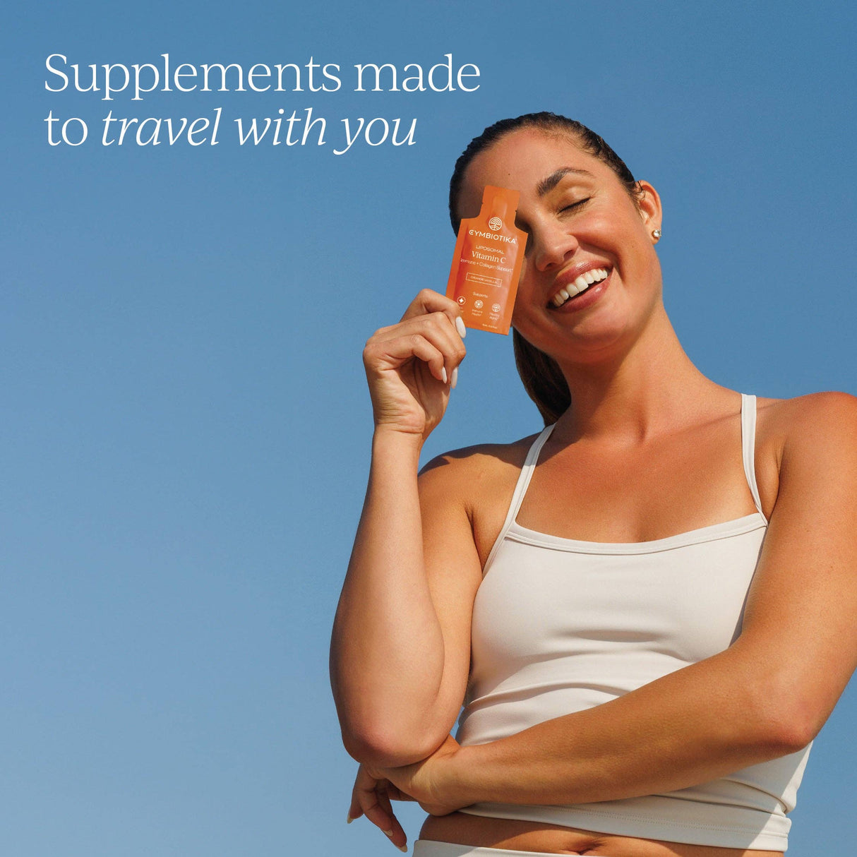 Woman holding a supplement bottle against a clear blue sky with text 'Supplements made to travel with you'.