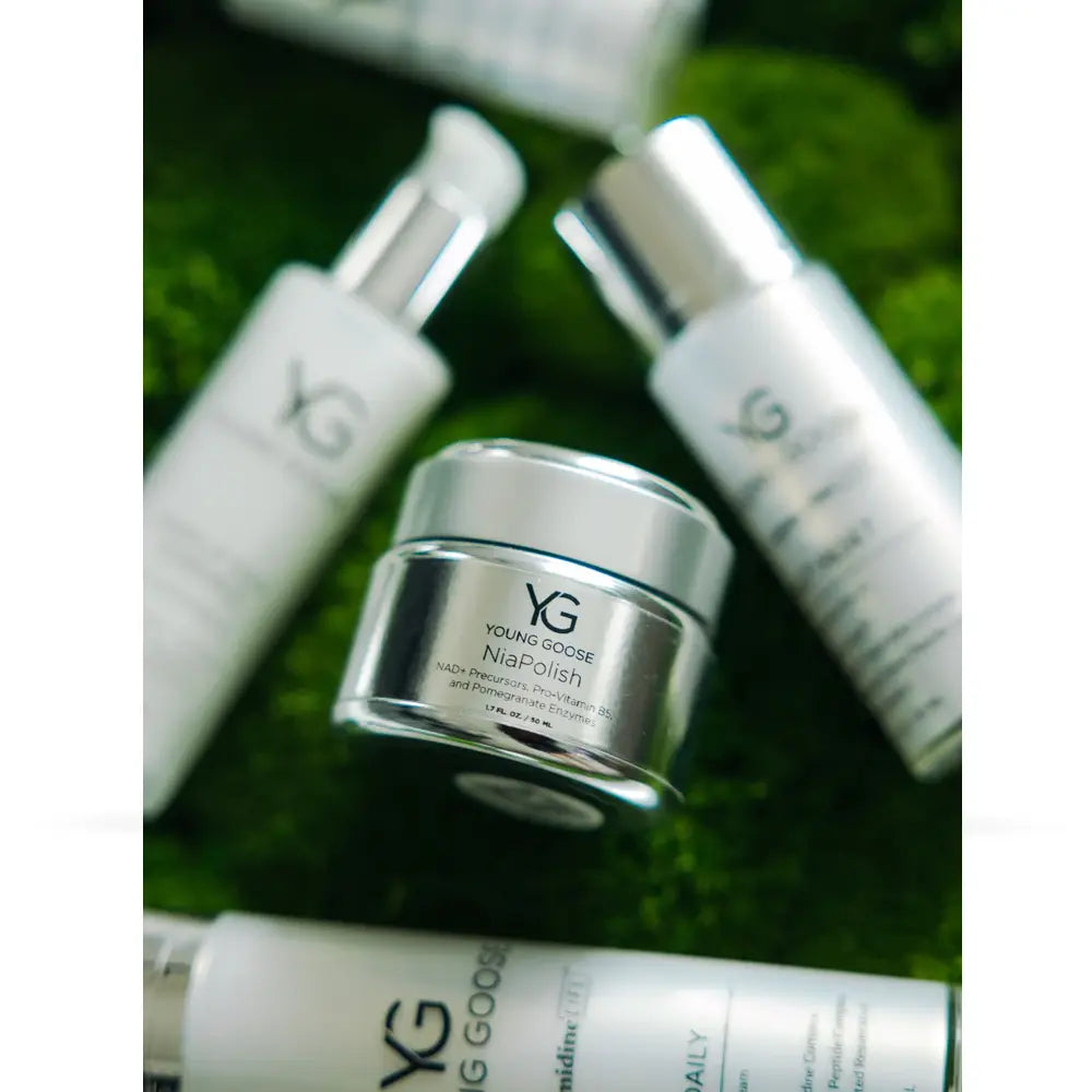 A collection of Young Gods skincare products, including a central silver jar of 'Night Polish' and other white bottles with silver caps, arranged on a textured green moss background.