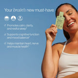A smiling woman in a white tank top holds up a small green tea supplement packet against a clear blue sky. Text on the left reads 'Your brain's new must-have' with three benefit bullet points and three icons.
