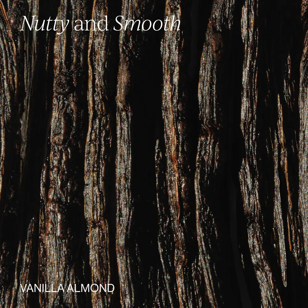 A close-up texture shot of dark vanilla almond bark with vertical grooves and glossy highlights, with the text 'Nutty and Smooth' at the top and 'VANILLA ALMOND' at the bottom in white.