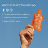 Hand holding a Cymbiotika vitamin C product against a blue background with text about immune system support.