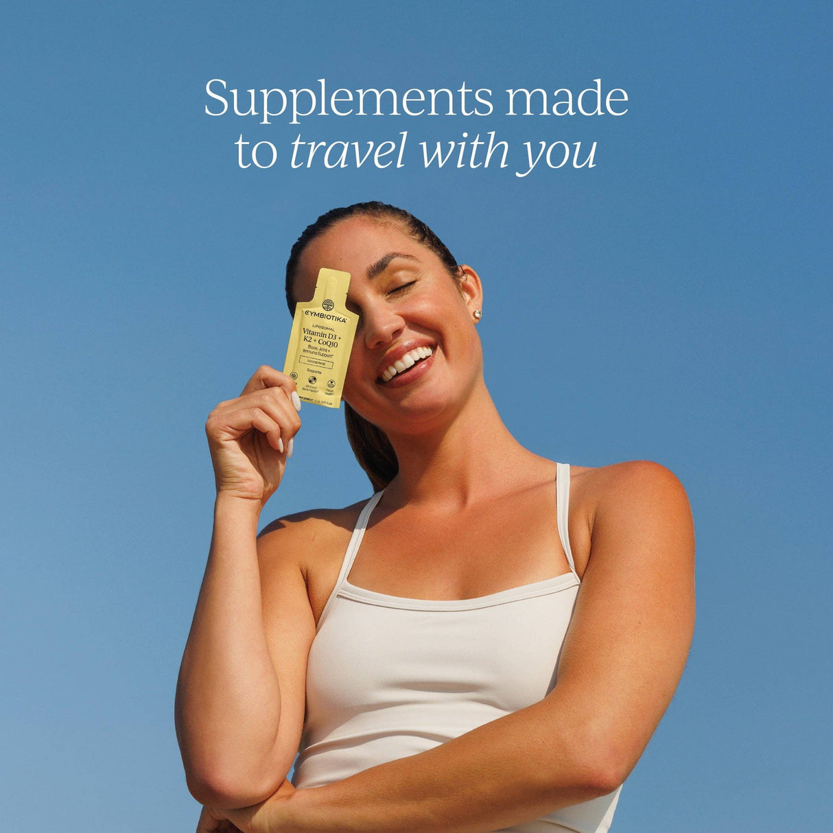 Woman holding a supplement bottle with a clear blue sky background and text 'Supplements made to travel with you'.