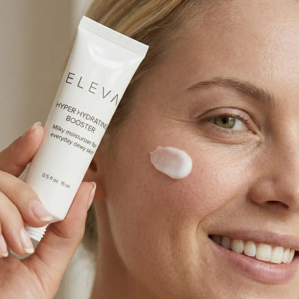 Woman with a dab of Elevai Hyper Hydrating Booster milky moisturizer on her cheek, holding the tube