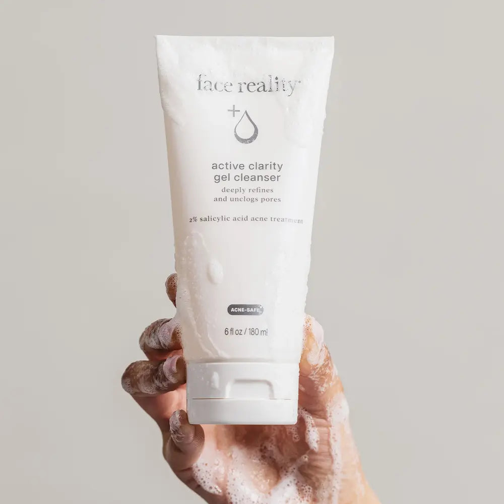 Hand with rich foam holding a tube of Face Reality Active Clarity Gel Cleanser