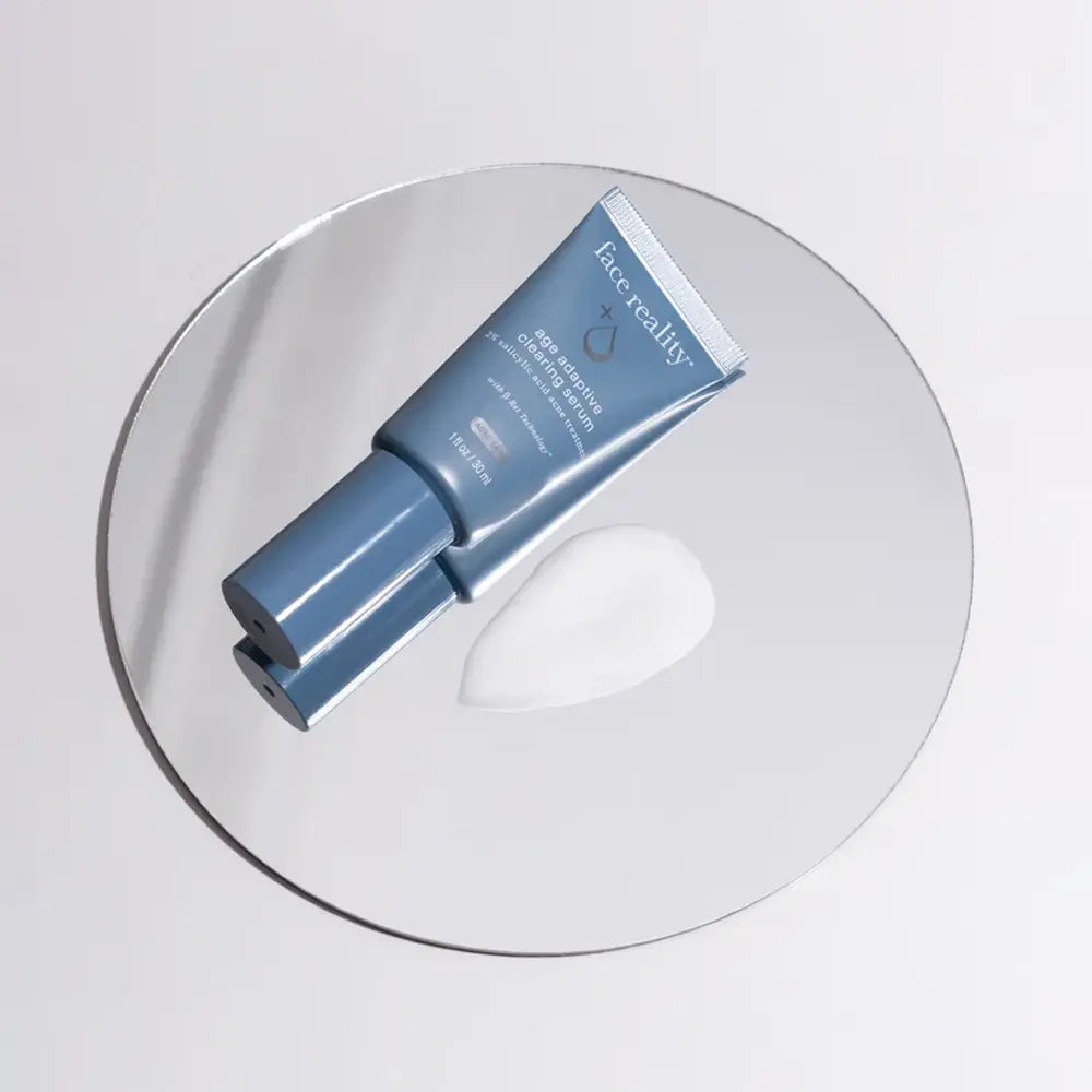 A Face Reality Age Adaptive Clearing Serum, placed diagonally on a round clear glass plate next to a dollop of product texture