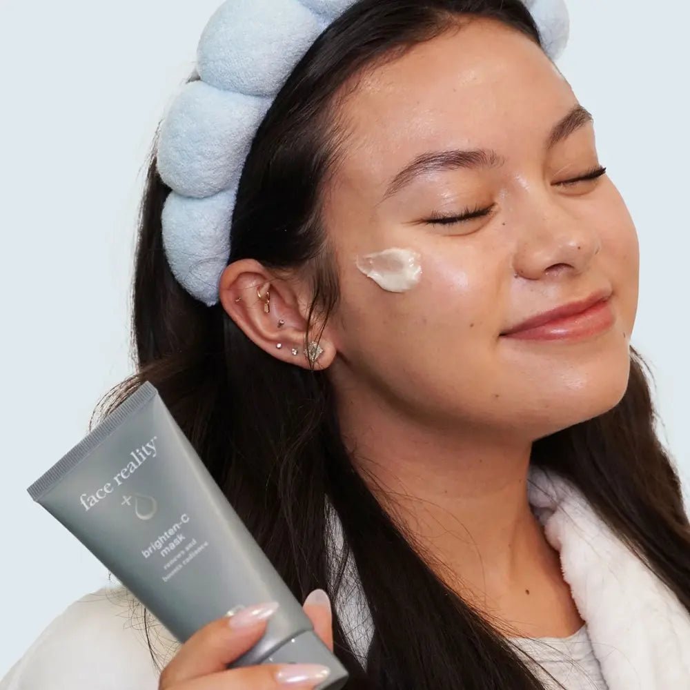 Woman applying cream to her face with a product labeled 'face reality' in the foreground.