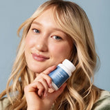 Woman holding a bottle of Face Reality Clear Skin Restore product against a blue background