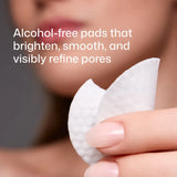 A close-up of a hand holding a Revision Skincare Tone+ Correcting Pad, with a blurred face in the background and text that reads: 'Alcohol-free pads that brighten, smooth, and visibly refine pores.'.