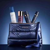 A Skinbetter Science Plump and Protect Daily Edit Set blue puffer-style cosmetic bag with a zipper and ribbon, shown with four skincare bottles and tubes protruding from the top. The bag has a visible Skinbetter logo patch.