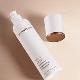 A white pump bottle of SKINMEDICA Even & Correct Advanced Brightening Treatment with gold lettering, shown next to its matching white cap with a metallic gold base on a warm beige background.
