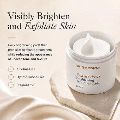 A white cosmetic jar of SkinMedica Even & Correct Brightening Treatment Pads sits on a beige stone slab with draped fabric. Text on the left reads 'Visibly Brighten and Exfoliate Skin' with product benefits listed below.
