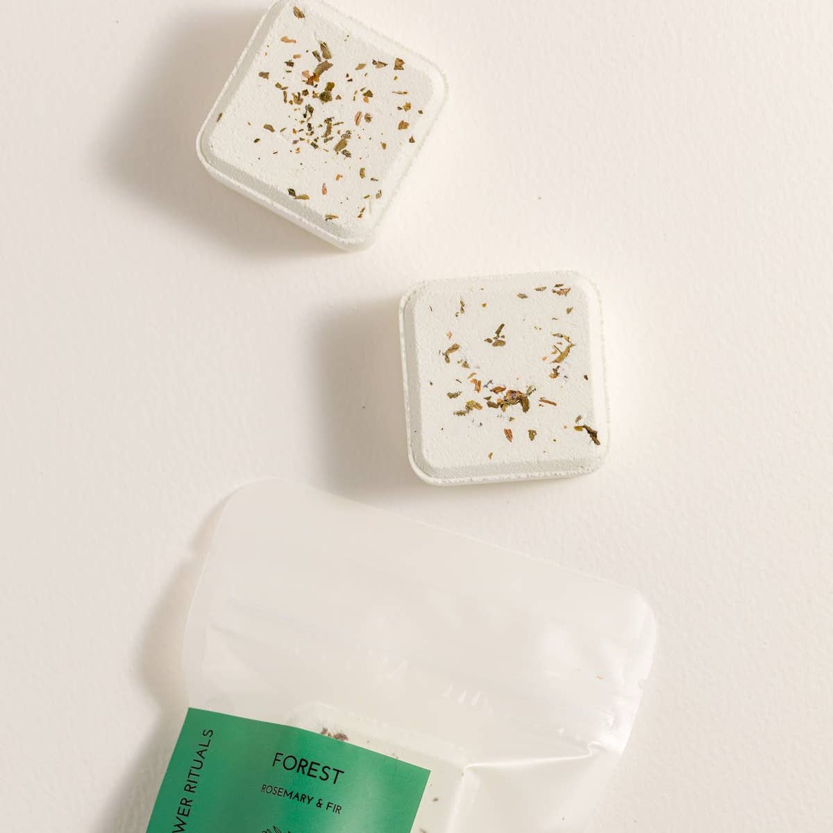 Two shower steamer tablets with decorative elements on a beige background, featuring a product labeled 'Forest'.