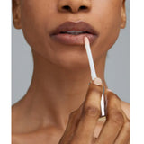 Close-up of a person applying a Young Goose Adaptogloss Anti-Aging Plumper with a doe-foot applicator, shown against a plain gray background.