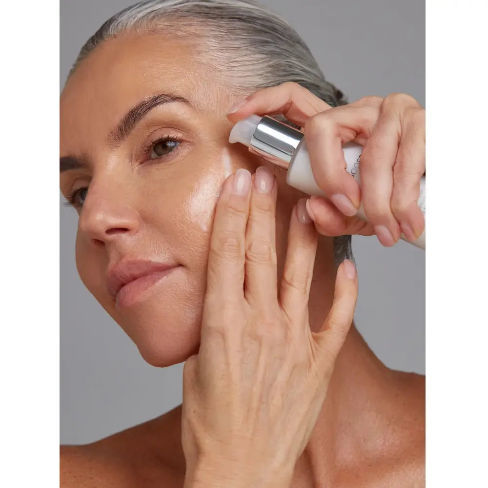 A close-up of a woman applying Young Goose Amplifying Essence to her cheek,