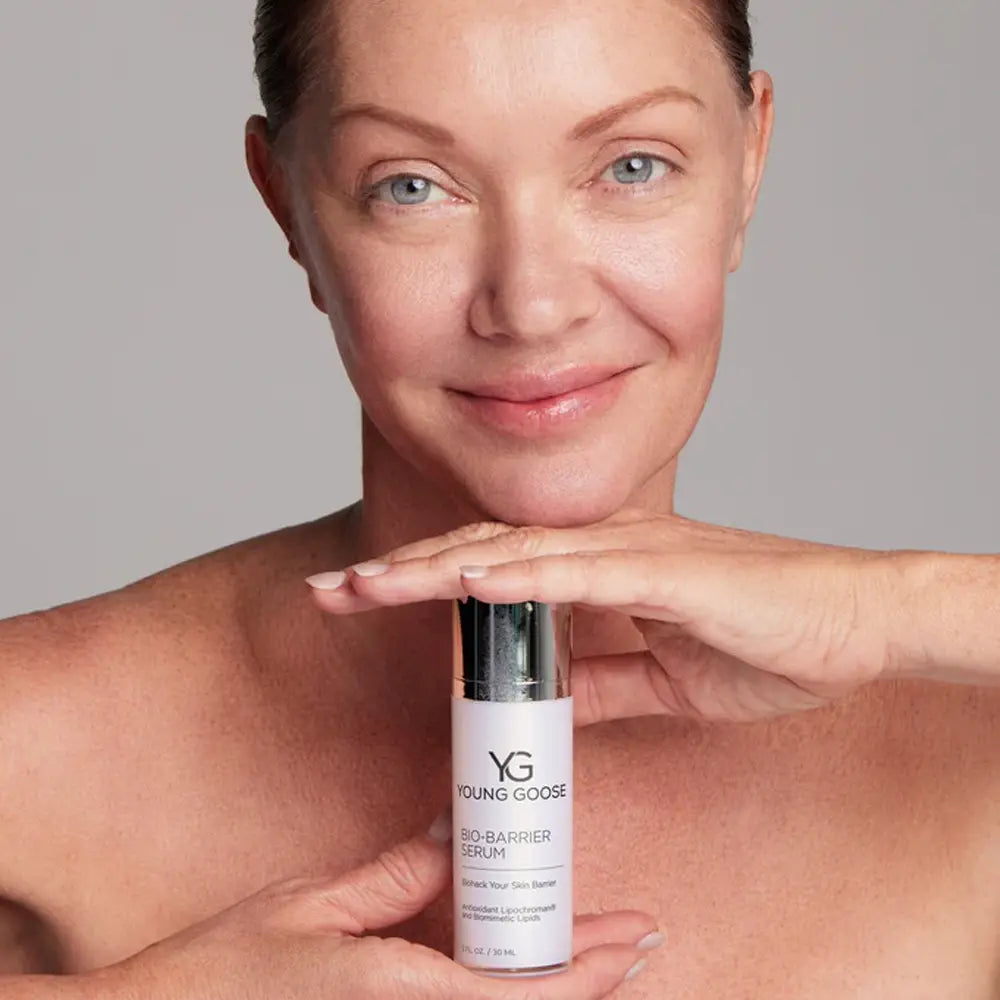 A woman holding a bottle of Young Goose Bio-Barrier Serum against a neutral gray background.