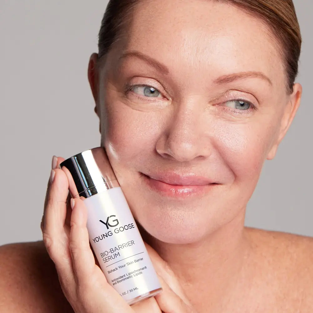 A close-up of a woman holding a bottle of Young Goose Bio Barrier Serum against a plain light gray background.