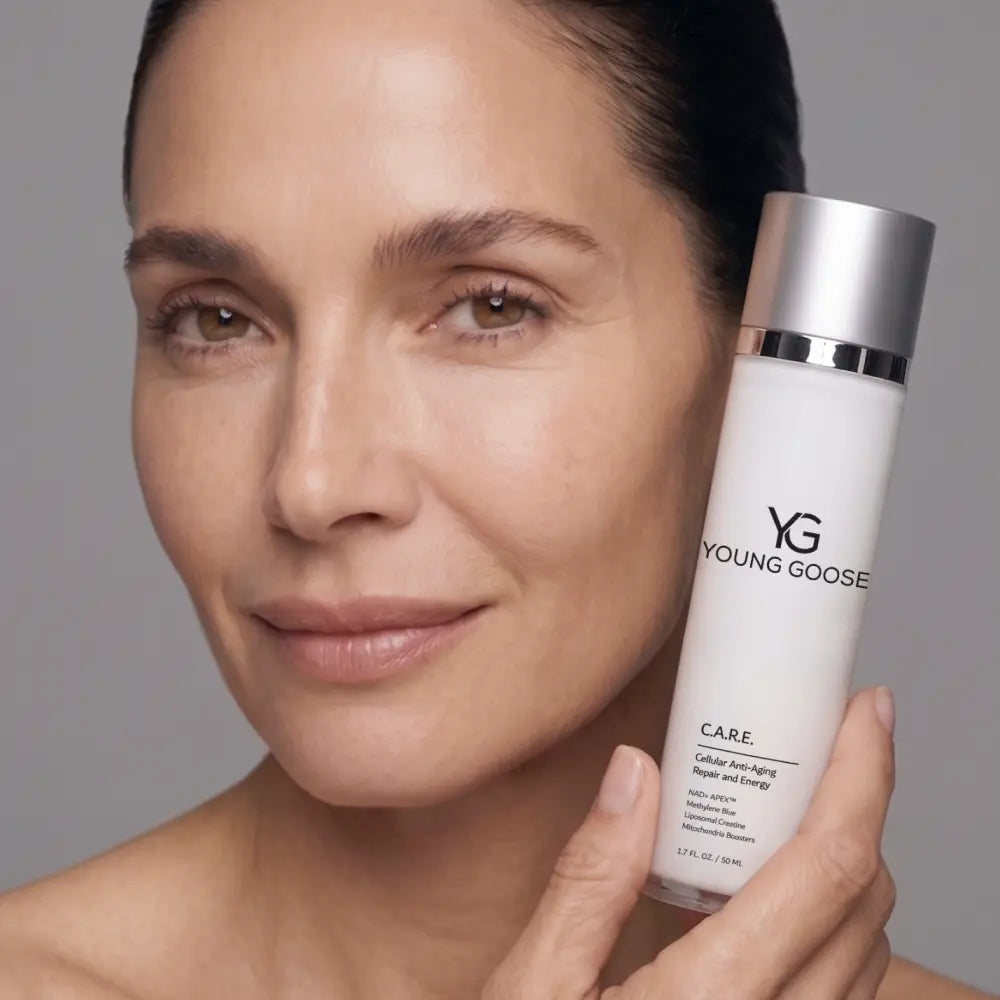 A close-up of a woman holding a bottle of Young Goose Care Cellular Renewing Serum against a neutral gray background.