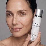 A close-up of a woman holding a bottle of Young Goose Care Cellular Renewing Serum against a neutral gray background.