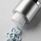 A close-up of Young Goose C.A.R.E. bottle dispensing a thick, pale blue cream onto a light gray surface.