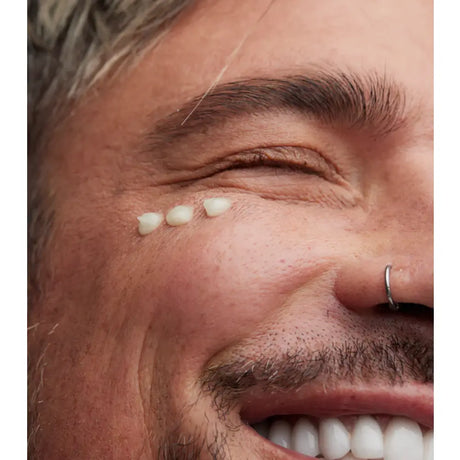 Close-up of a smiling man's face with three small white dots of Young Goose EyeC.A.R.E. serum placed in a row under his eye