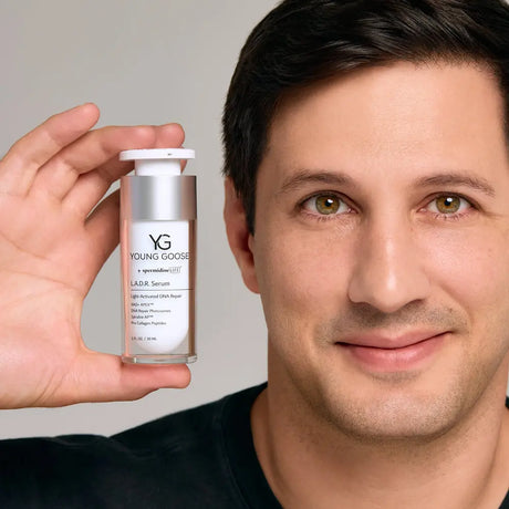 A close-up of a man holding up a bottle of Young Goose L.A.D.R. Serum against a neutral light gray background.