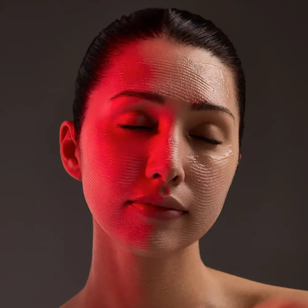 Close-up portrait of a woman with closed eyes, her face illuminated by dramatic red lighting against a dark gray background with Young Goose L.A.D.R. Serum in her face