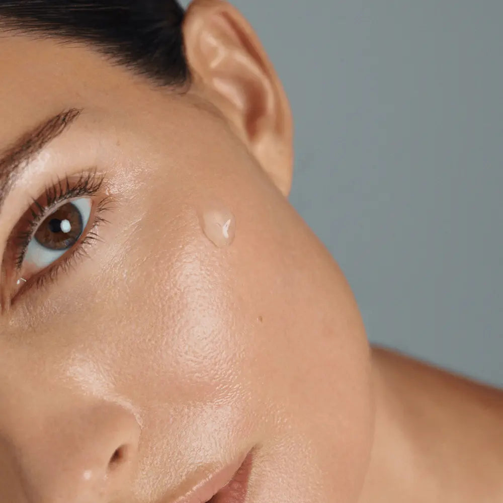 Close-up of a woman's face with Young Goose Vampire Exosomes drop on her cheek against a soft gray background.