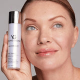 A close-up of a woman holding a bottle of Young Goose Youth Daily Moisturizing Cream next to her face, showing the product packaging and its use in skincare.