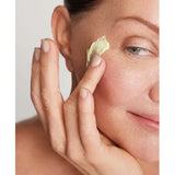 Close-up of a woman applying Young Goose Youth Daily to her cheek with her finger, shown against a soft light gray background.