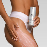 A close-up of a model's hip and thigh applying a pinkish cream while holding a silver can of Young Goose Youth Firming Body Cream against a light gray background.